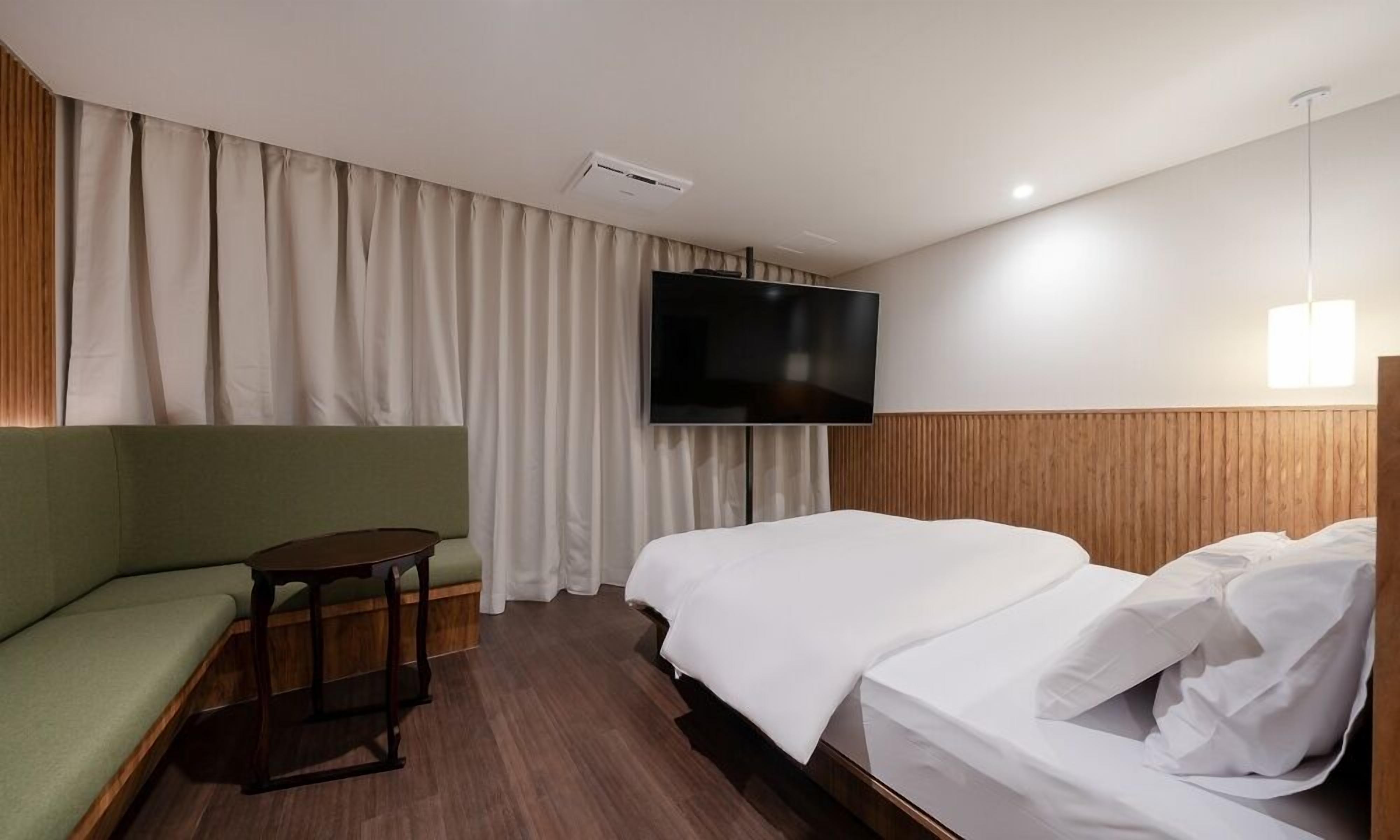 A hotel room with a bed, a green sofa, a small table, and a TV mounted on the wall.