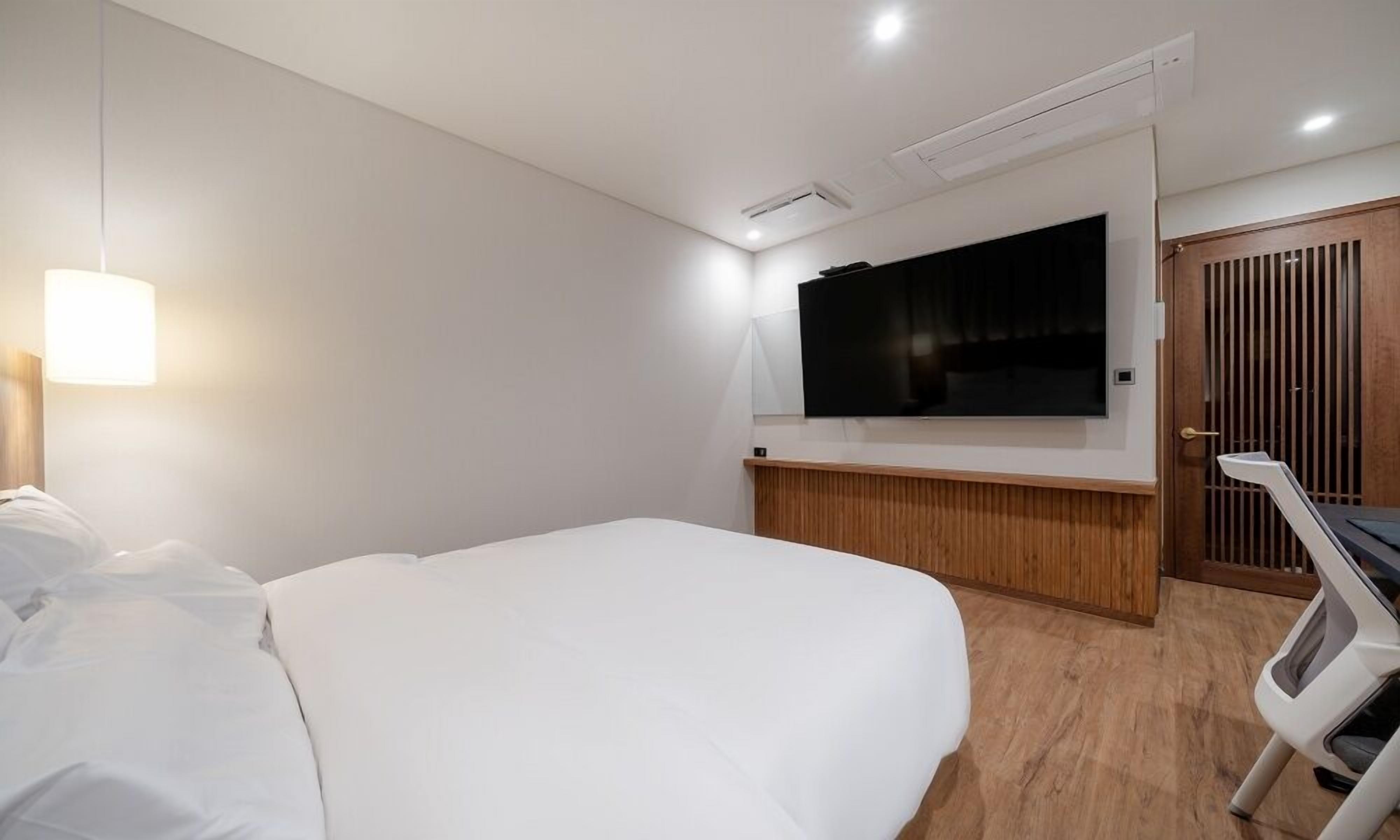 Ett modernt hotellrum med en stor säng, en platt-TV som är monterad på väggen och en dörr av trä.