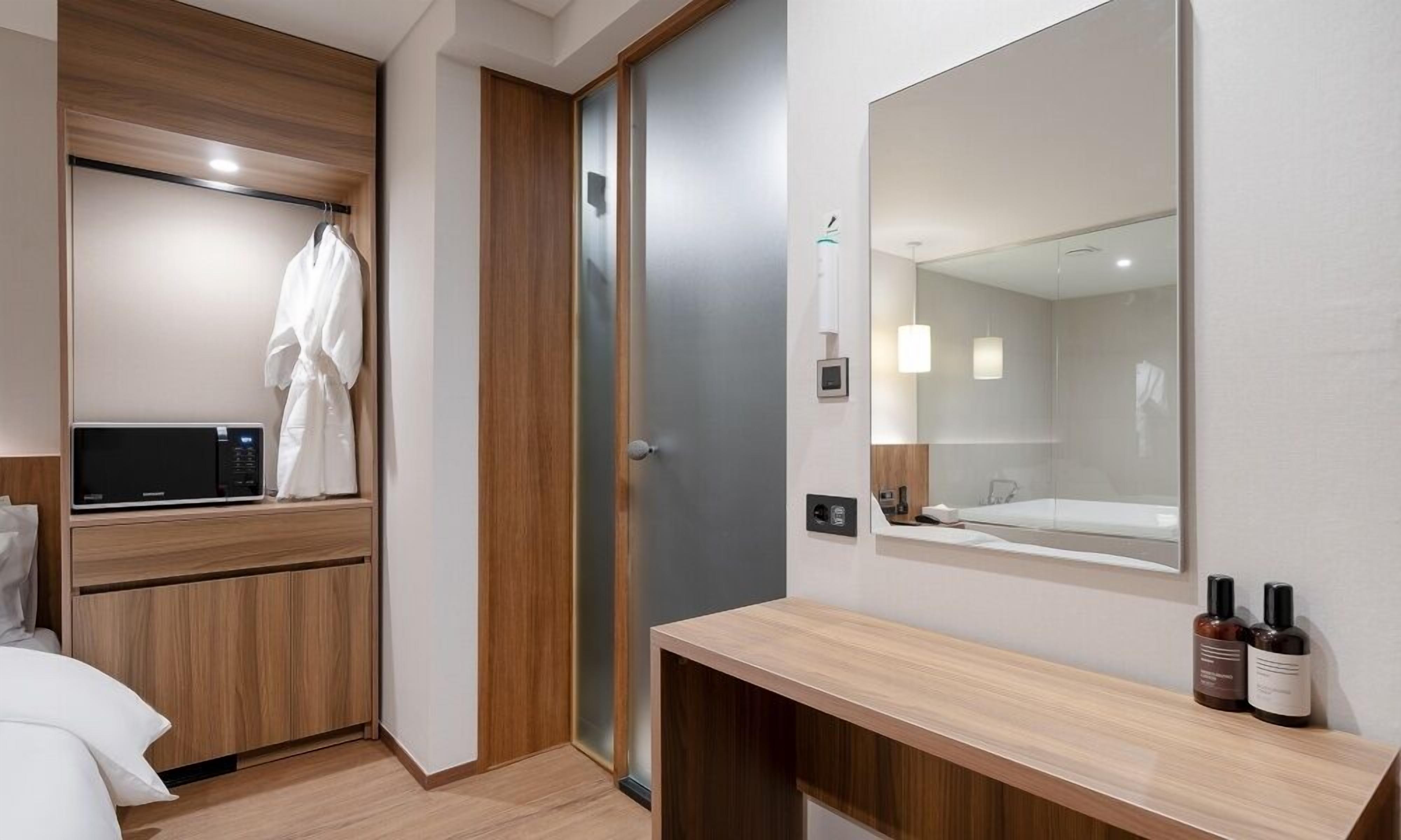 A modern hotel room with a wooden vanity, a large mirror, and a shower area.