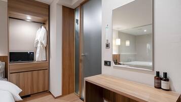 A modern hotel room with a wooden vanity, a large mirror, and a shower area.