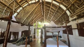 A room with a thatched roof, wooden beds, and a fan.