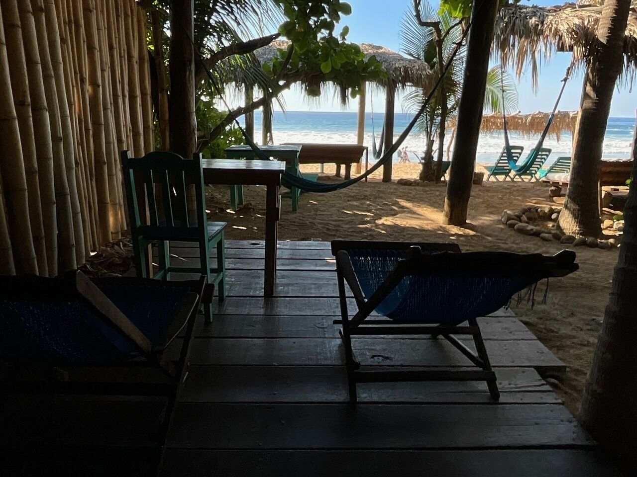 Una terraza de madera con dos hamacas, una mesa y sillas, con vista a una playa.