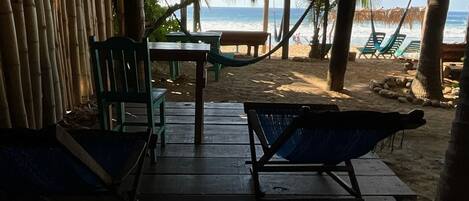 Una terraza de madera con dos hamacas, una mesa y sillas, con vista a una playa.