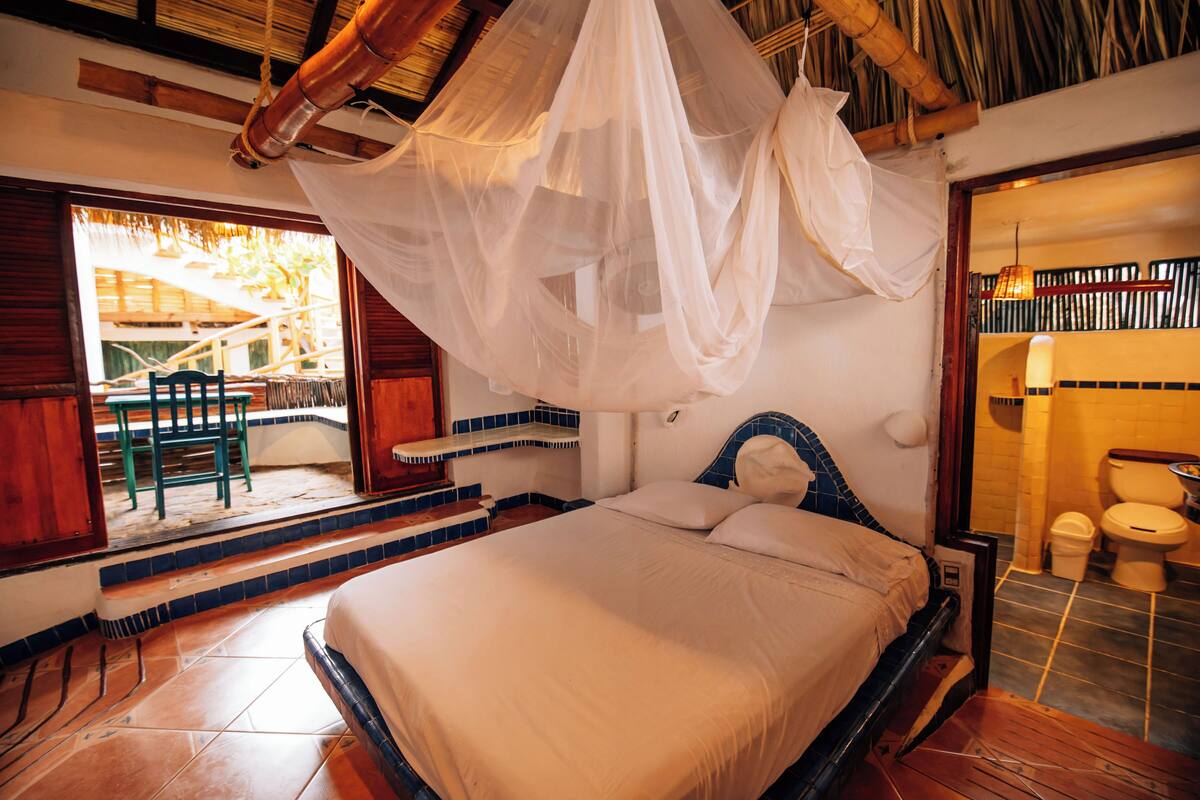 A bed with a canopy, a bathroom with a toilet and sink, and a view of the outside.