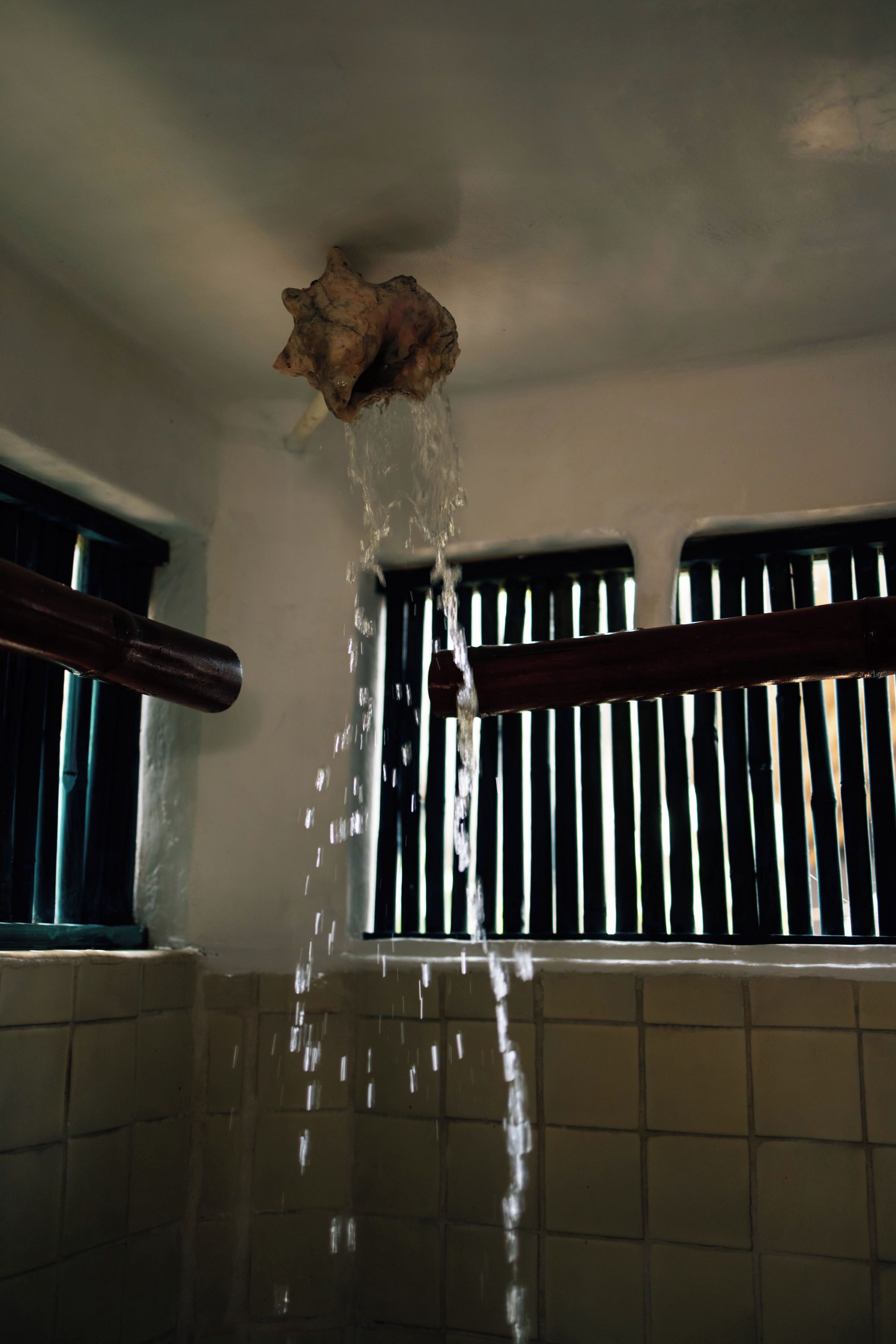 A bathroom with a shower area, tiled walls, and a window with bars.