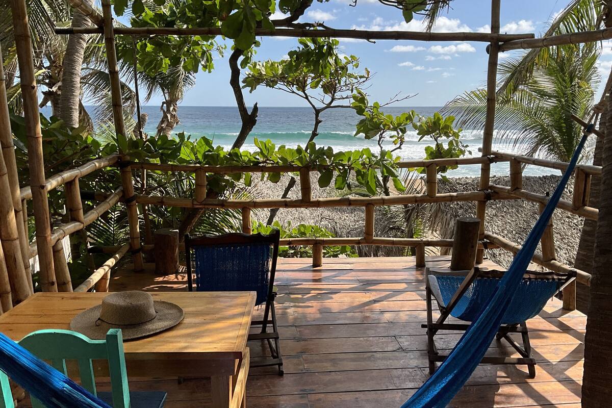 A wooden deck with a table and chairs, a hammock, and a view of the ocean.
