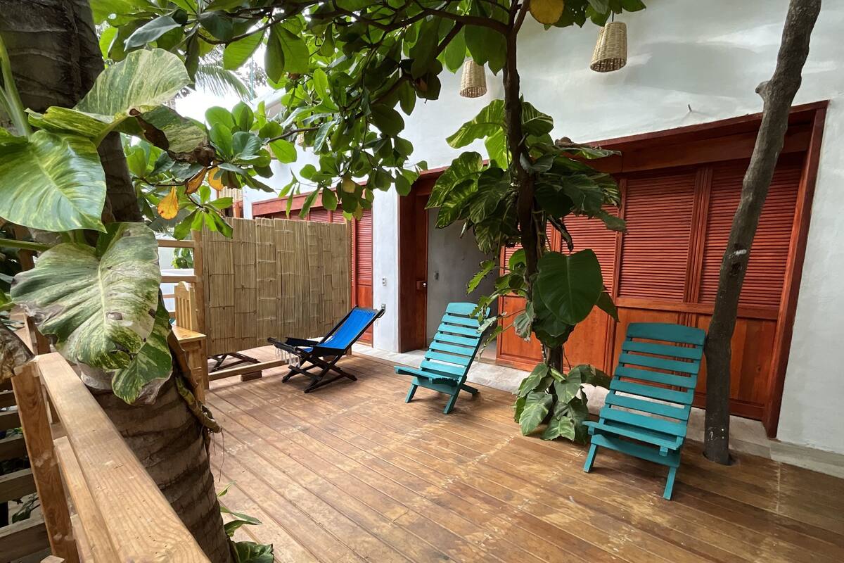 A wooden deck with two blue lounge chairs, a wooden table, and large green plants.