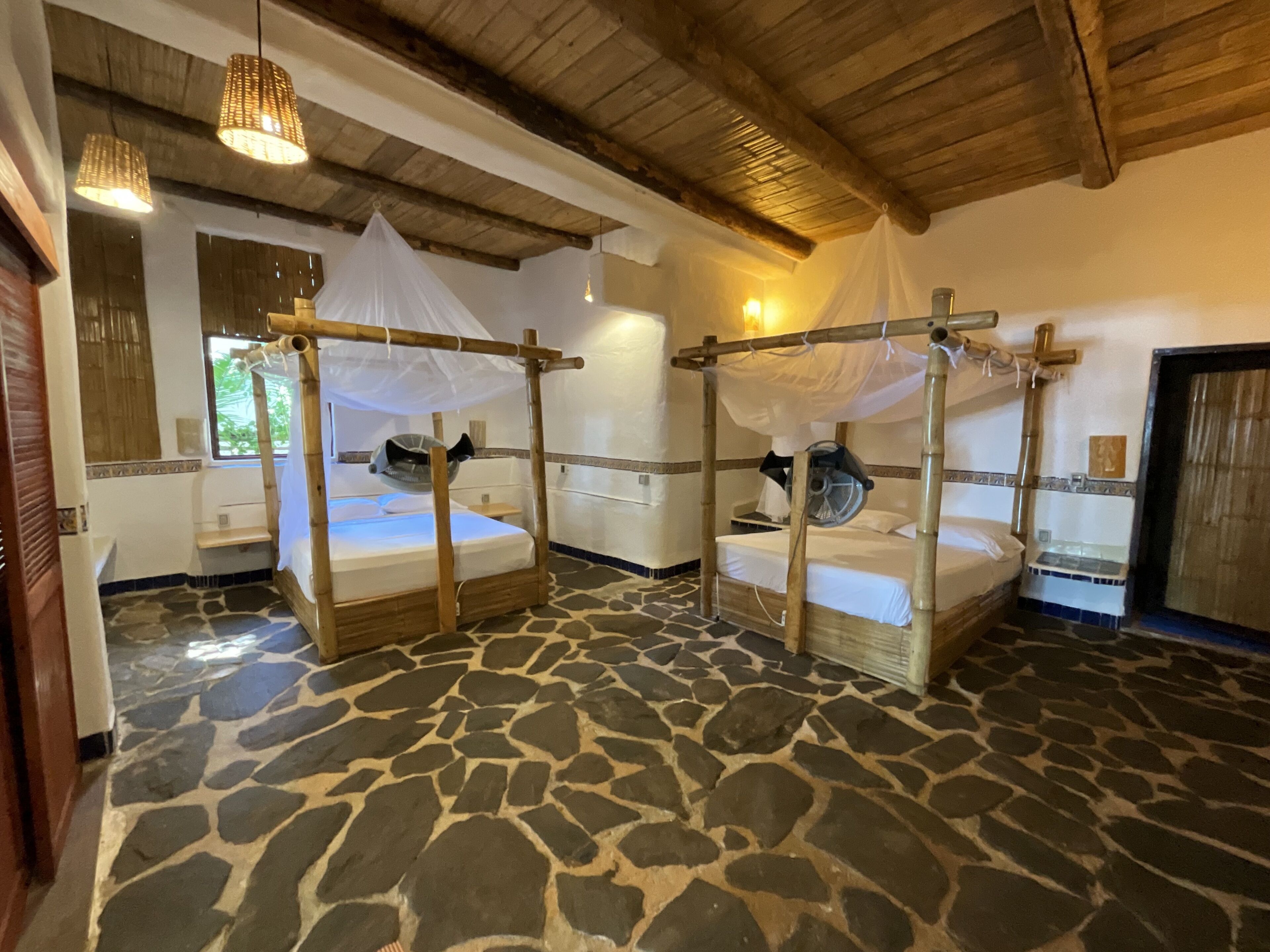 A room with four beds, each with a canopy, and a stone floor.