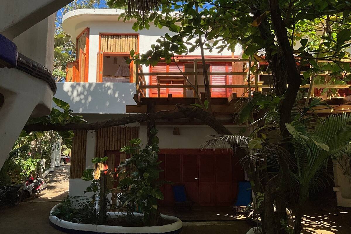 A courtyard with a two-story building, a covered seating area, and a variety of plants.