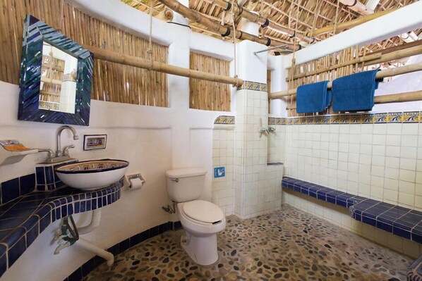A bathroom with a white toilet, a blue and white tiled sink, a mirror with a decorative frame, and a bamboo ceiling. - BAMBU Ecocabanas (Santa María Tonameca)