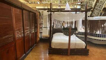 A traditional room with a thatched roof, a wooden bed with a mosquito net, and a wooden wardrobe.