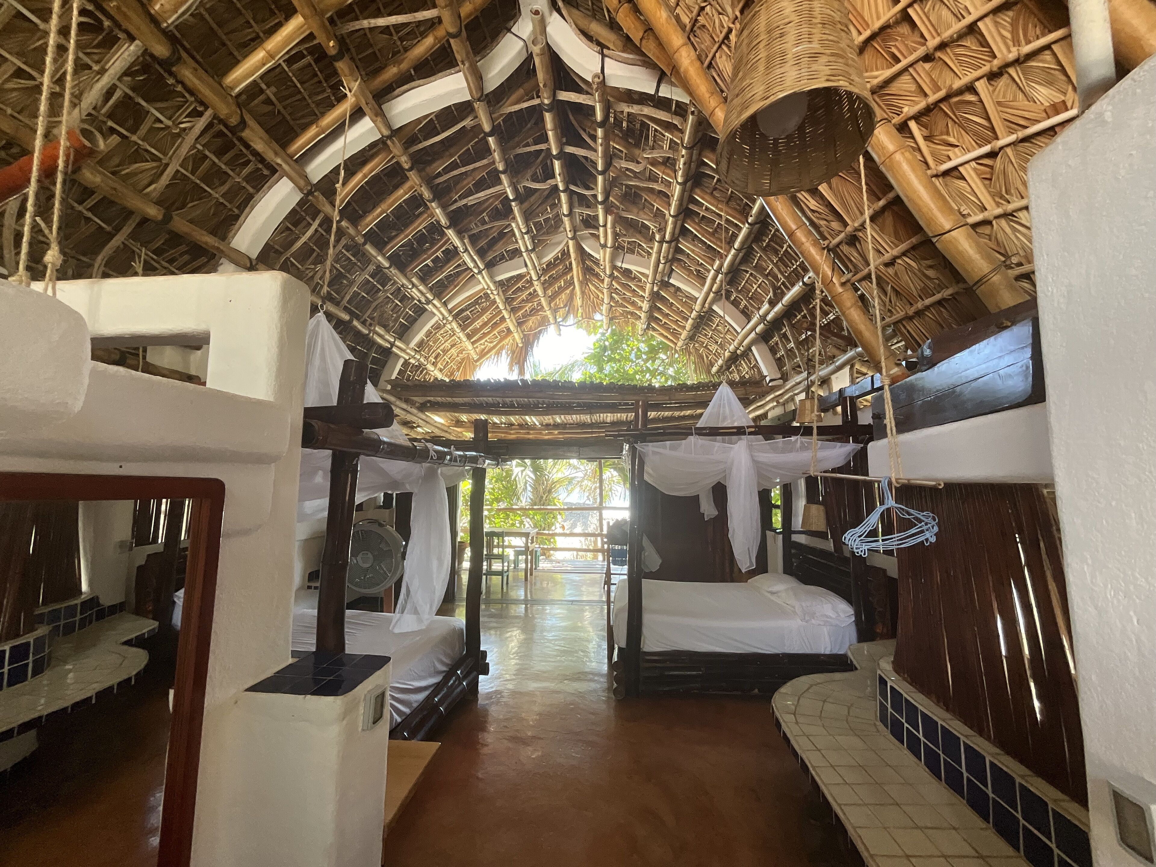 Quarto com teto de bambu, cama, ventilador e vista para o exterior.