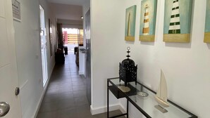 Un couloir doté d’un sol carrelé, une table en verre ornée d’un objet décoratif et trois tableaux représentant des phares accrochés au mur.