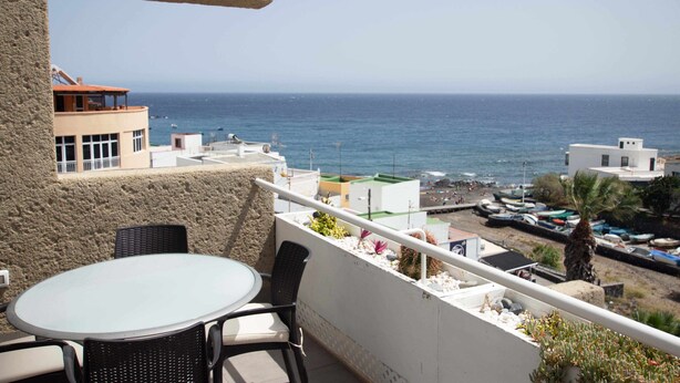 Un balcon avec une table et des chaises donnant sur une zone côtière, avec des bateaux et des bâtiments.