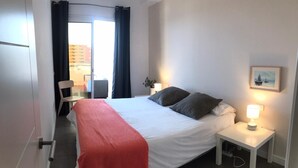 Une chambre d’hôtel avec un lit, une table de chevet avec une lampe, une chaise et une vue sur les bâtiments environnants.