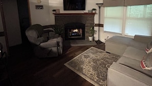 A living room with a fireplace, a ceiling fan, and a television mounted on the wall.