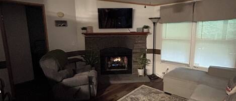 A living room with a fireplace, a ceiling fan, and a television mounted on the wall.