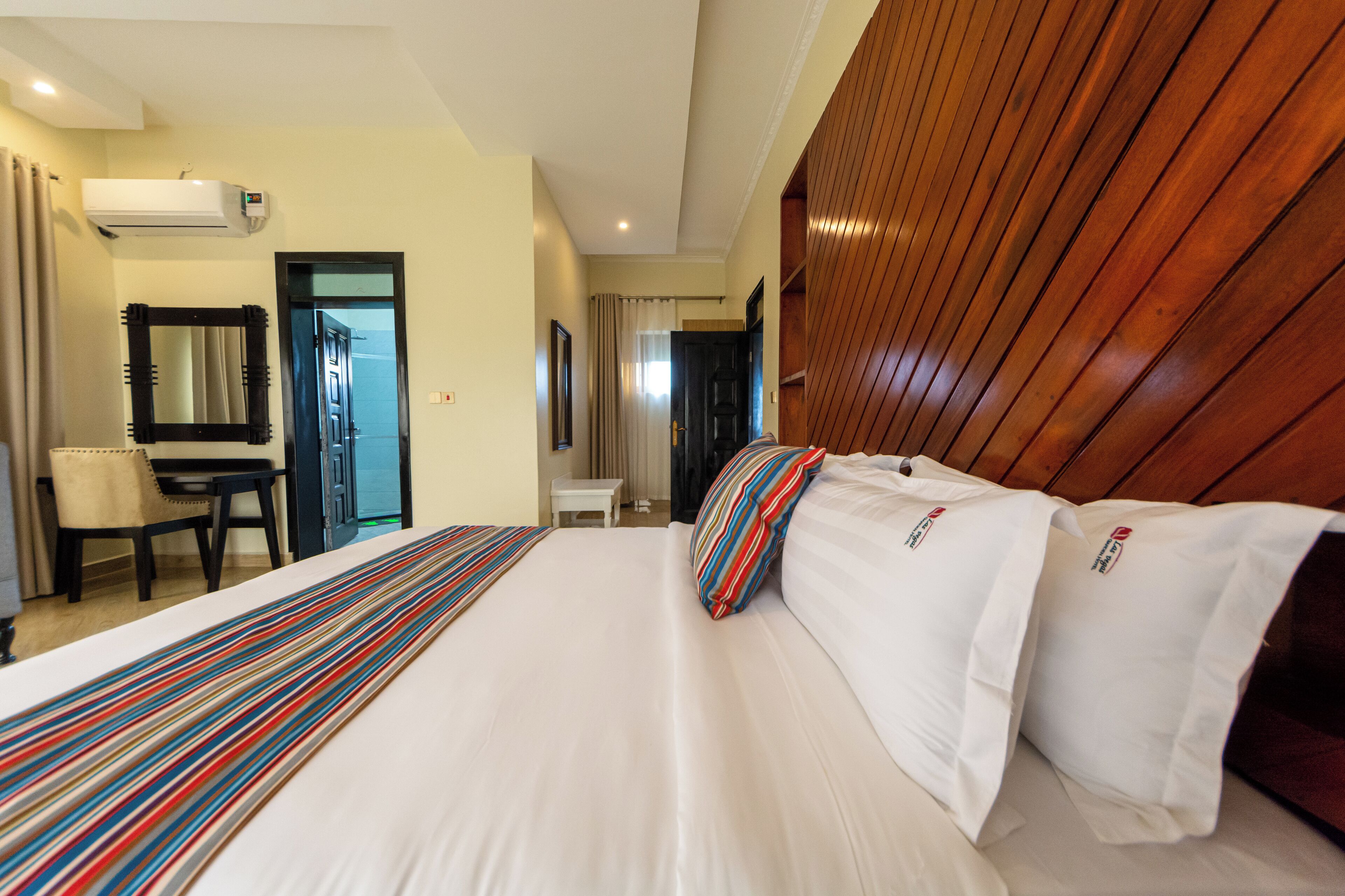 A hotel room with a large bed, a wooden headboard, a desk, and a chair.