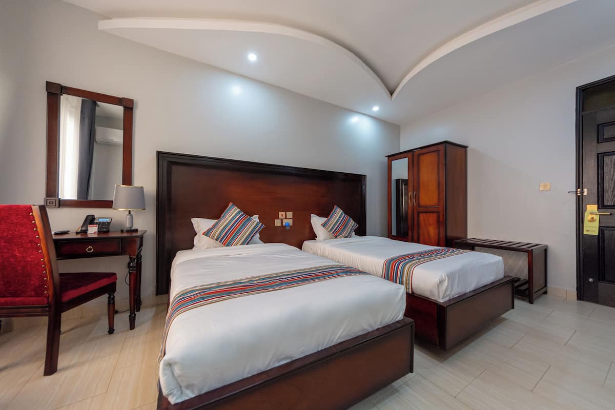 Habitación de hotel con dos camas, un escritorio con teléfono, una silla, un espejo y un armario.