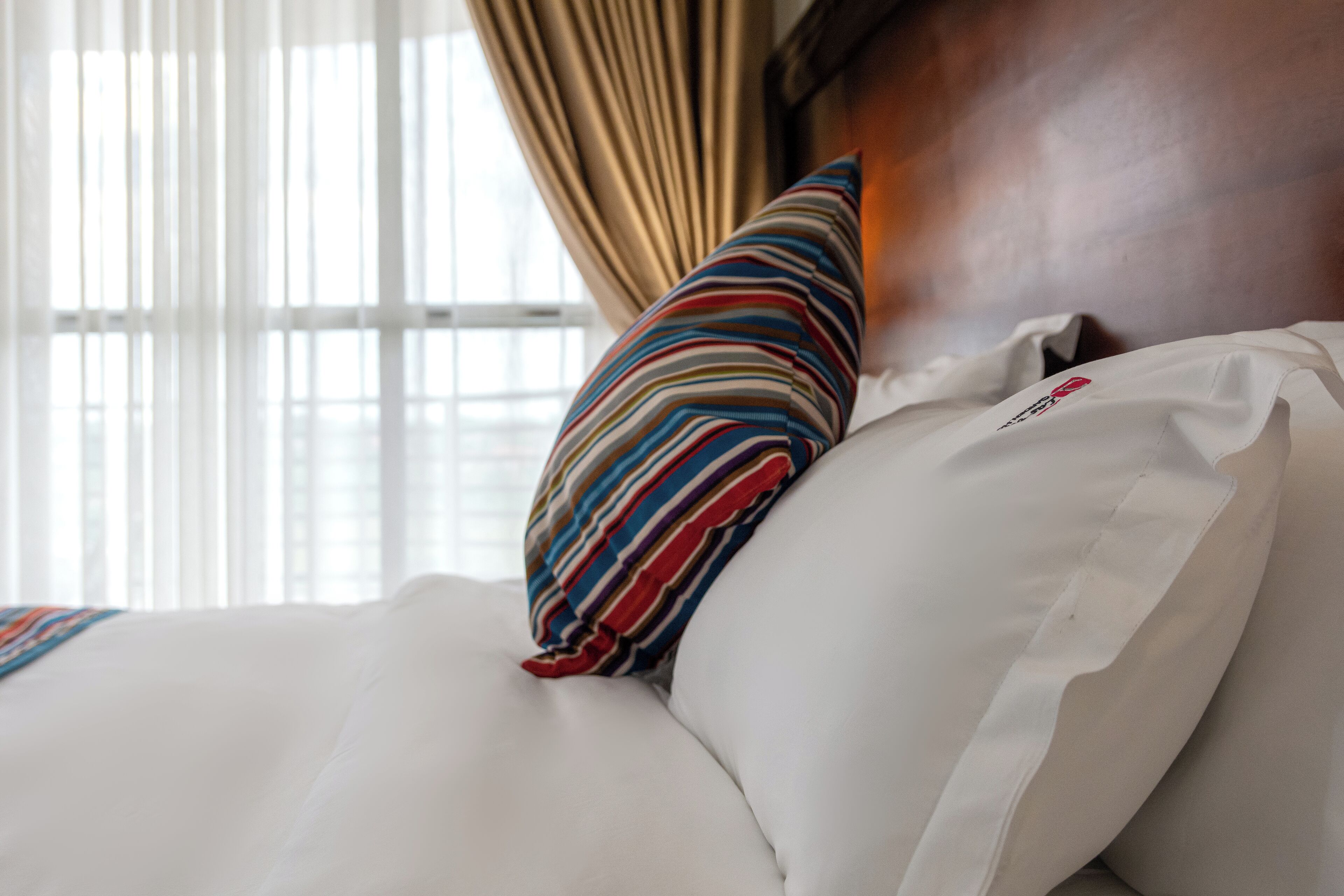 Een hotelbed met witte lakens, een gestreept kussen en een houten hoofdbord.