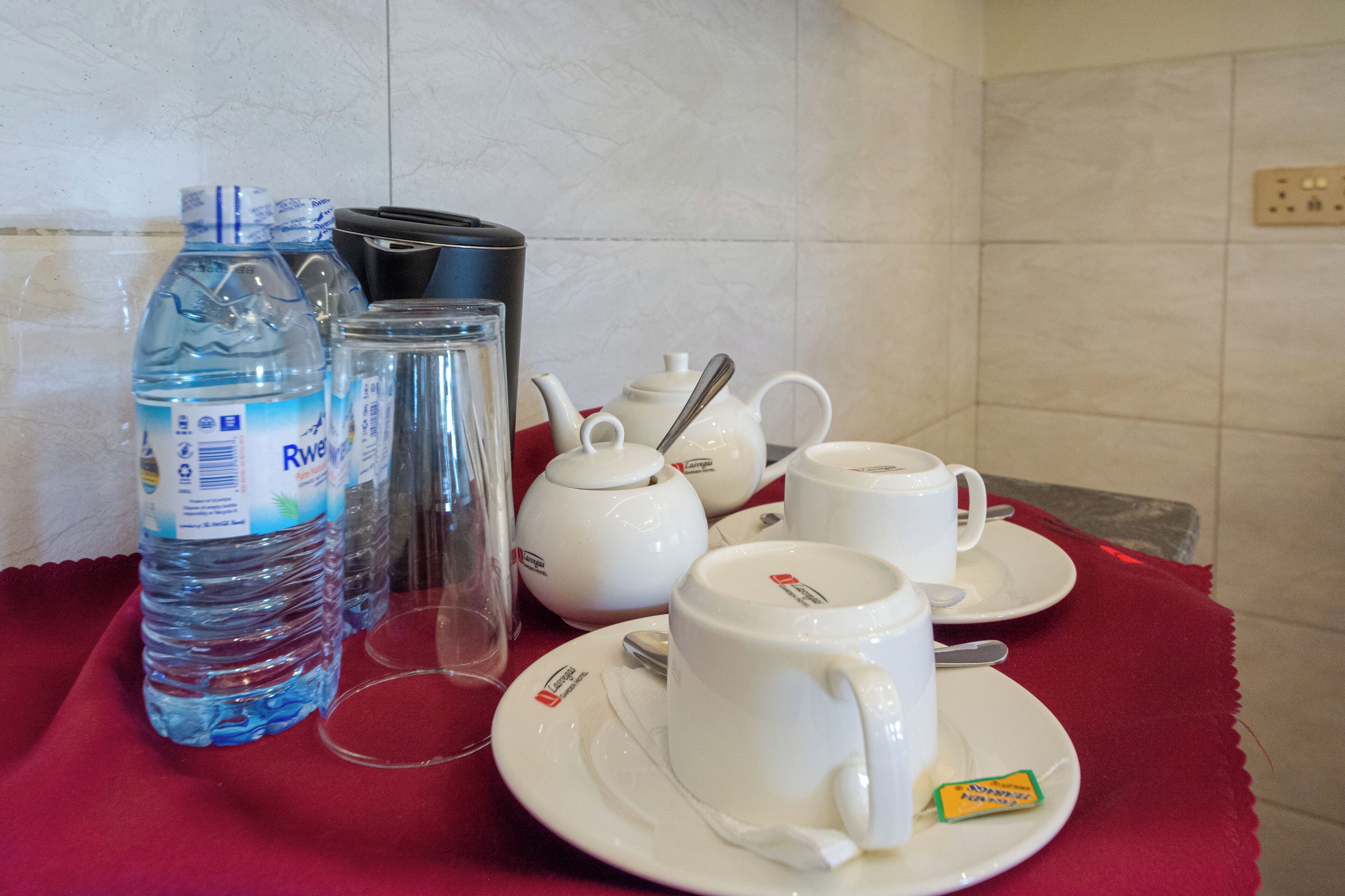 Una mesa dispuesta con teteras blancas, tazas, platillos y una tetera con cuchara. También hay botellas de plástico transparente y un vaso.