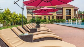 Zona junto a la piscina con sillones de descanso y sombrillas rojas.