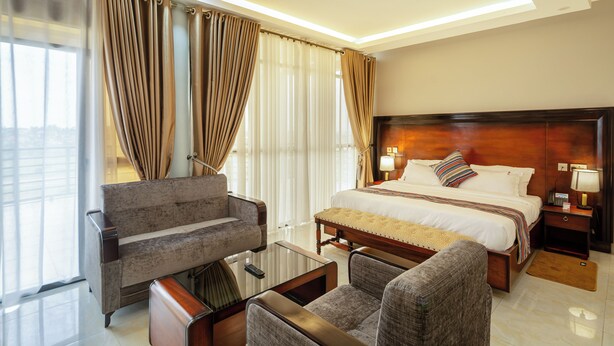 A hotel room with a large bed, a sofa, a coffee table, and a desk with a lamp. - Las Vegas Hotel Mbarara (Mbarara)