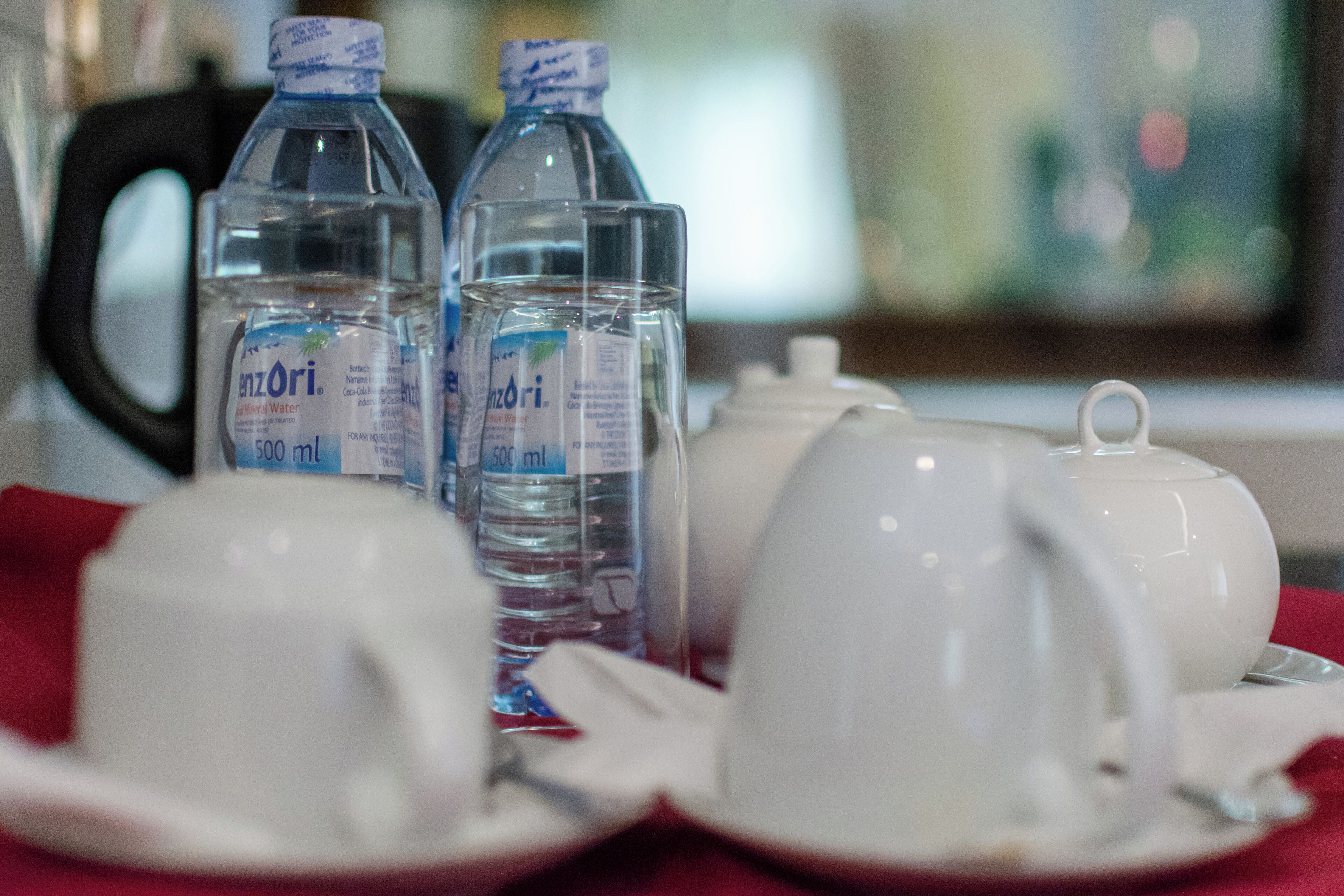 Una mesa dispuesta con tazas de té blancas, platillos y una tetera, junto con dos botellas de agua con la etiqueta 'Hanzori' y capacidad de 500 ml.