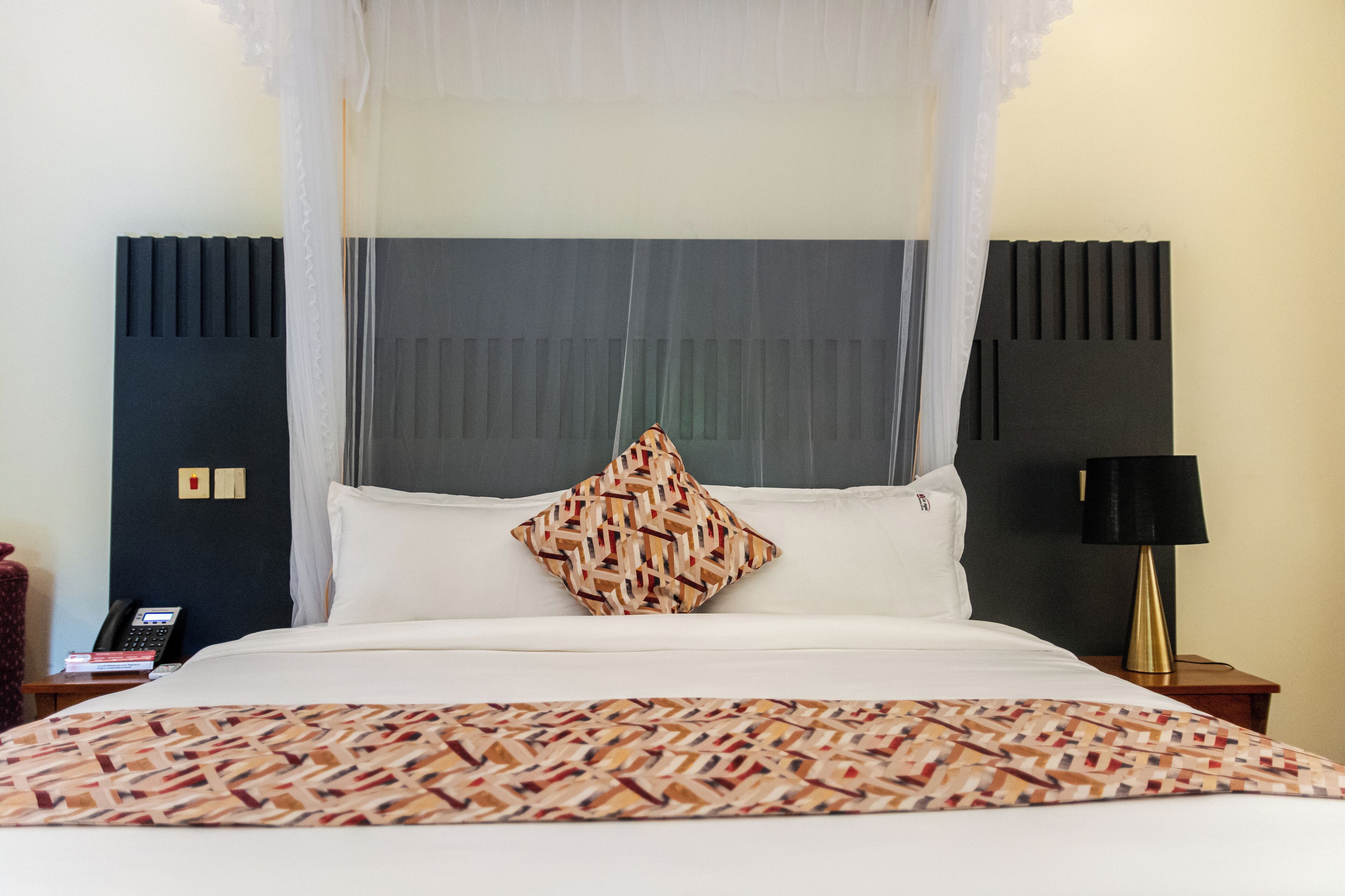 A hotel room with a bed, a bedside table with a lamp, and a telephone.