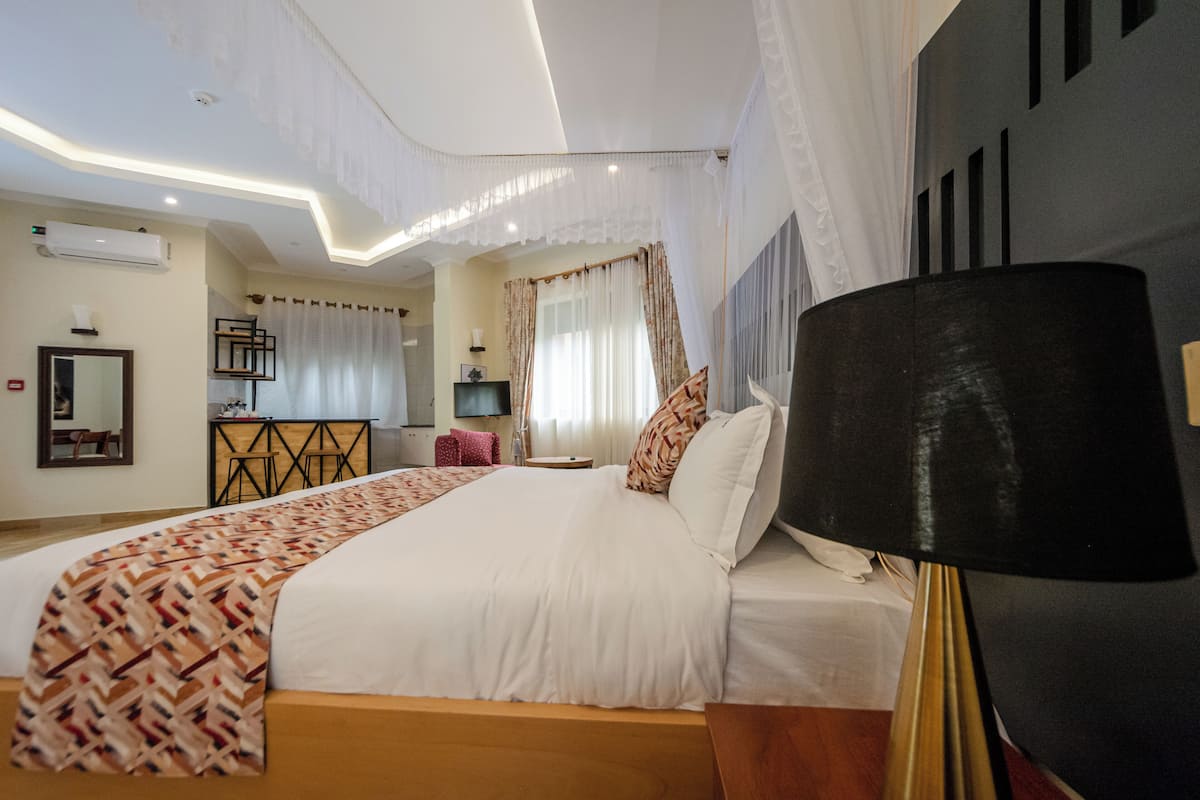 Habitación de hotel con una cama grande, un escritorio, una silla, un televisor y una lámpara en el techo.