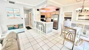 Una cocina moderna con una isla central, azulejos blancos y una zona de comedor con una mesa de vidrio y sillas de madera.