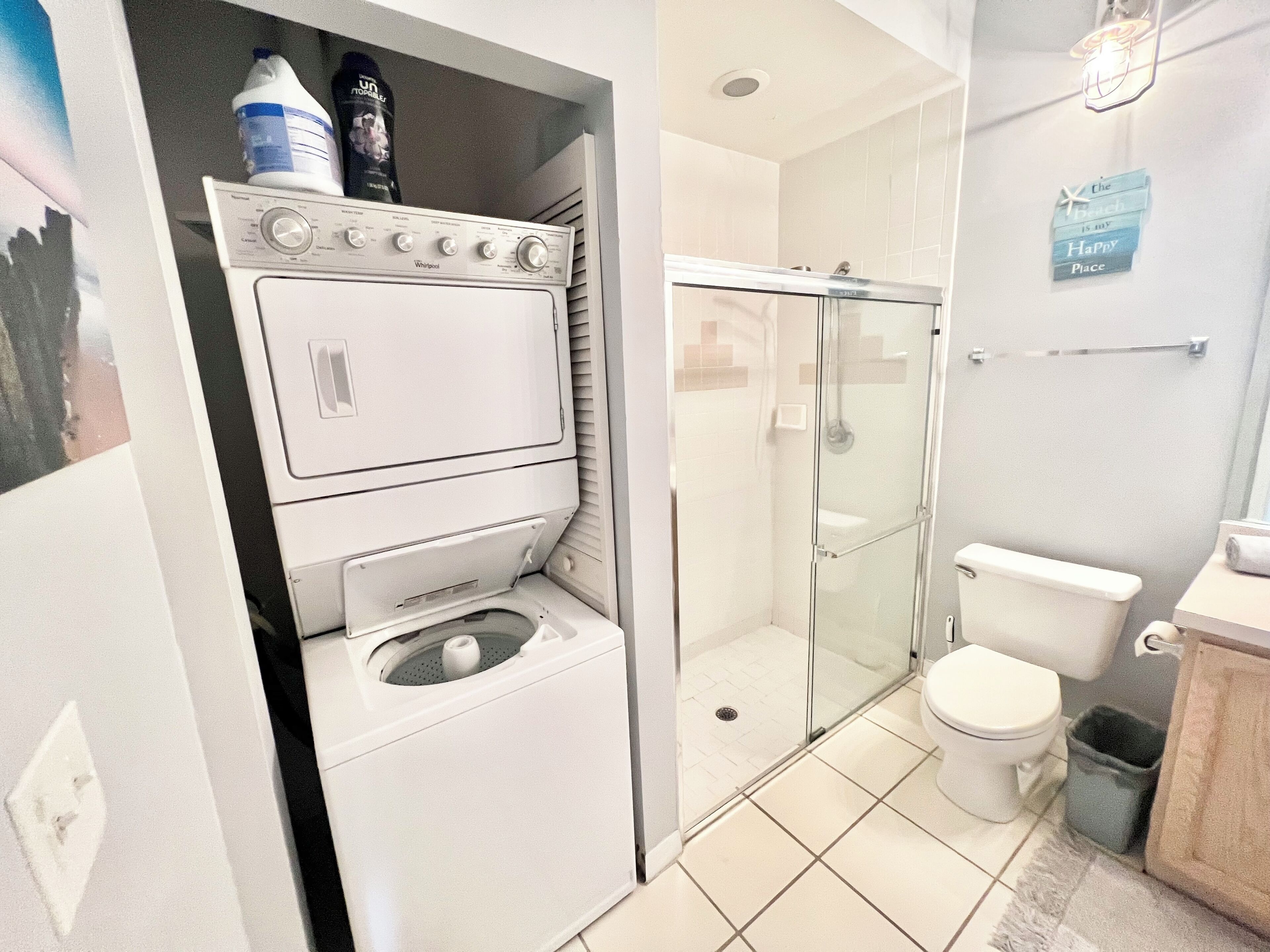 A compact bathroom with a washing machine, a glass-enclosed shower, and a toilet.