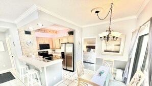 Una cocina moderna con una isla central, electrodomésticos de acero inoxidable y un comedor con mesa de vidrio y sillas de madera.