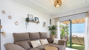 A modern living room with a sofa, two small round tables, and a large sliding glass door leading to an outdoor area with a view of the sea. - Cozy Apartment with Sea Views in Costa Adeje (Adeje)