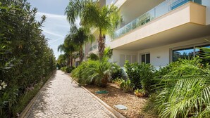 A pathway lined with greenery and a modern building with balconies. - Luxury Apt. Garden, Pool and Near Beach (Lagos)