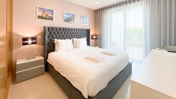 A modern hotel room with a large bed, two bedside tables, a desk, and a large window with curtains. - Luxury Apt. Garden, Pool and Near Beach (Lagos)