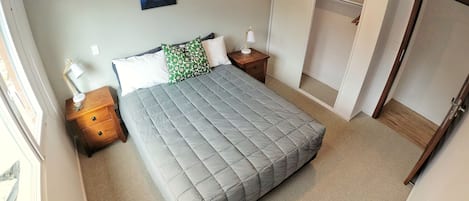 A neatly arranged bedroom with a bed, bedside tables, a nightstand, a wardrobe, and a painting on the wall.
