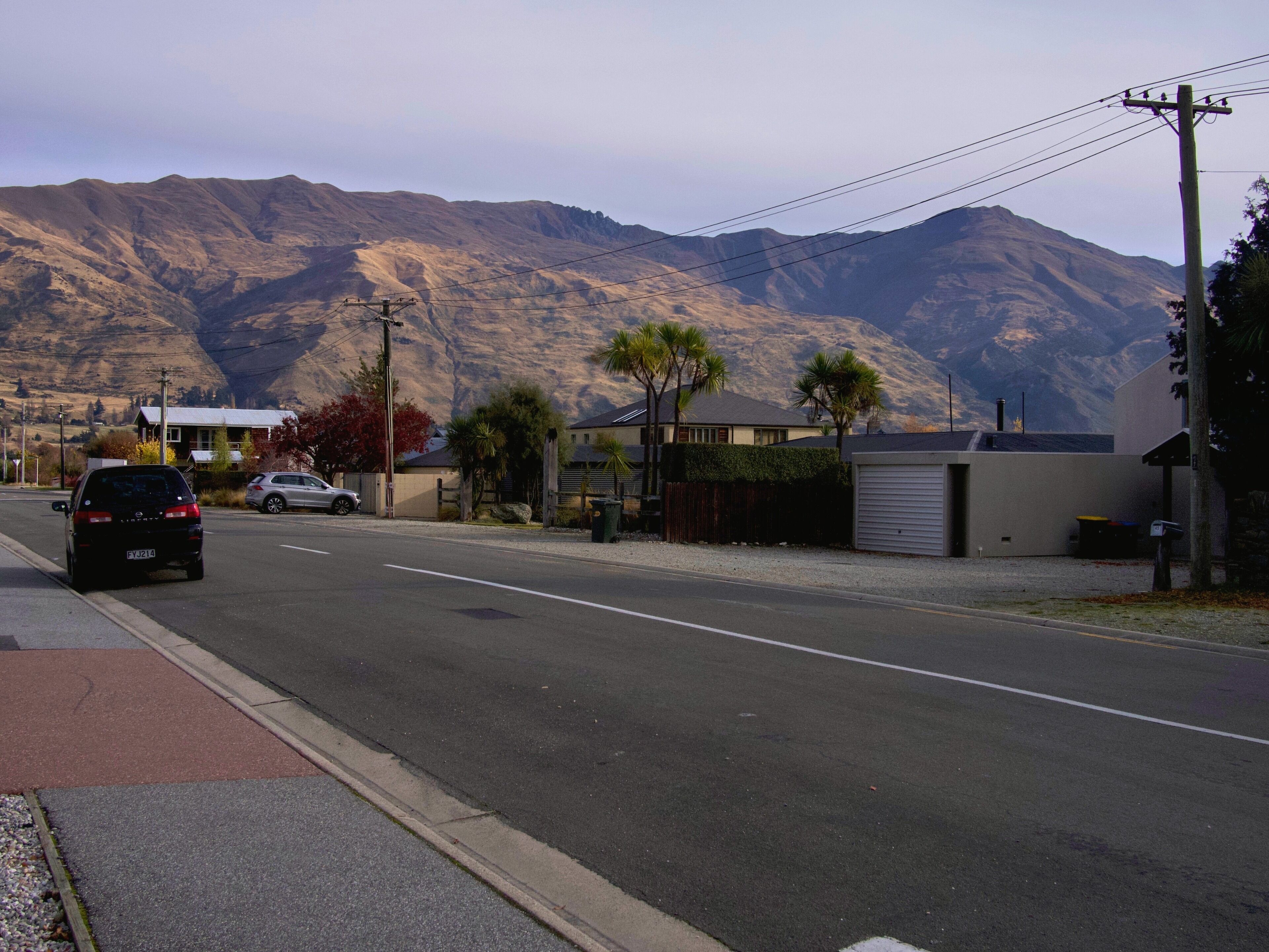 A street with houses, a car, and mountains in the background.