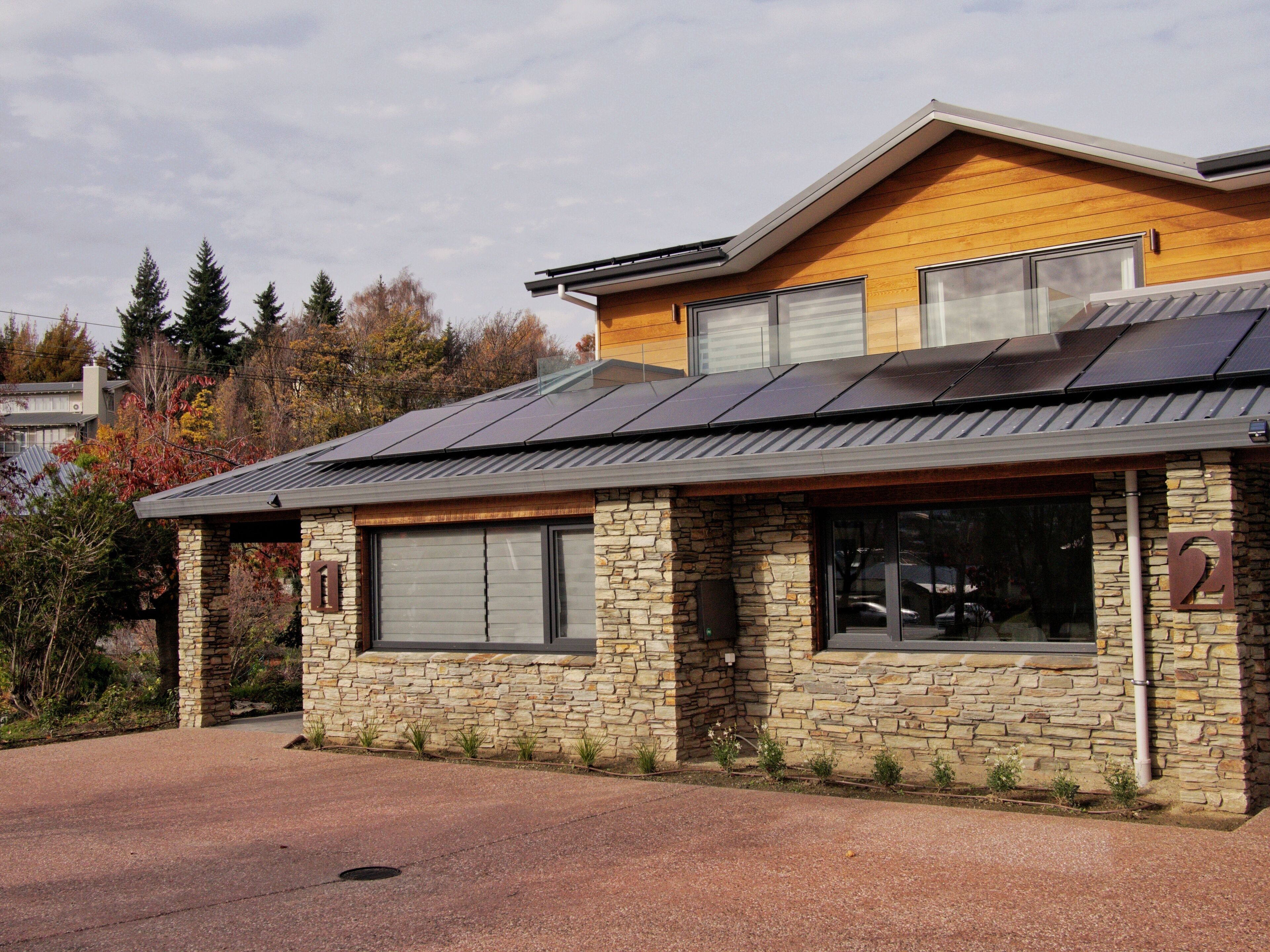 A modern building with a stone facade, large windows, and a sloped metal roof.