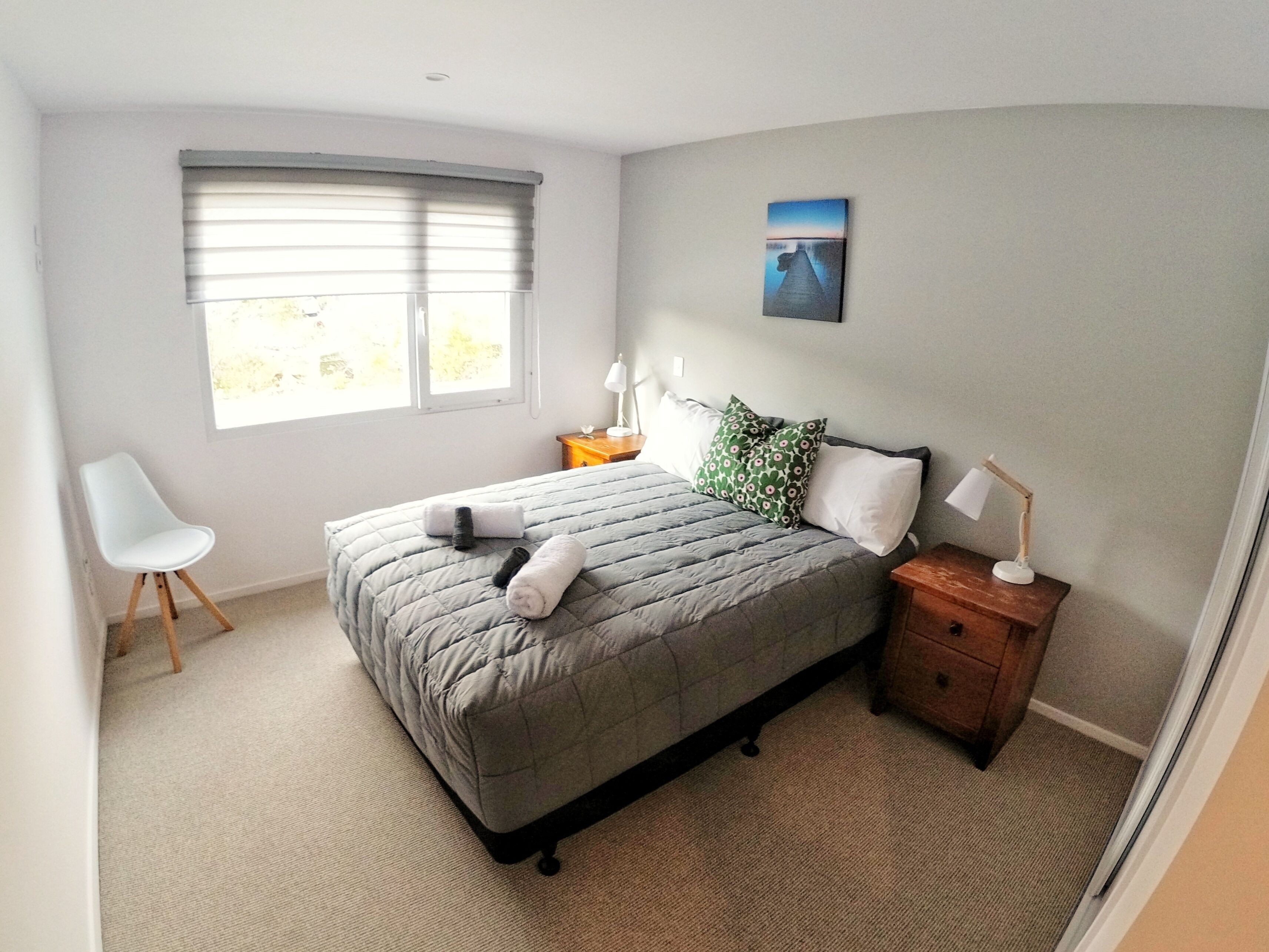 A bedroom with a bed, a chair, a nightstand with a lamp, and a painting on the wall.