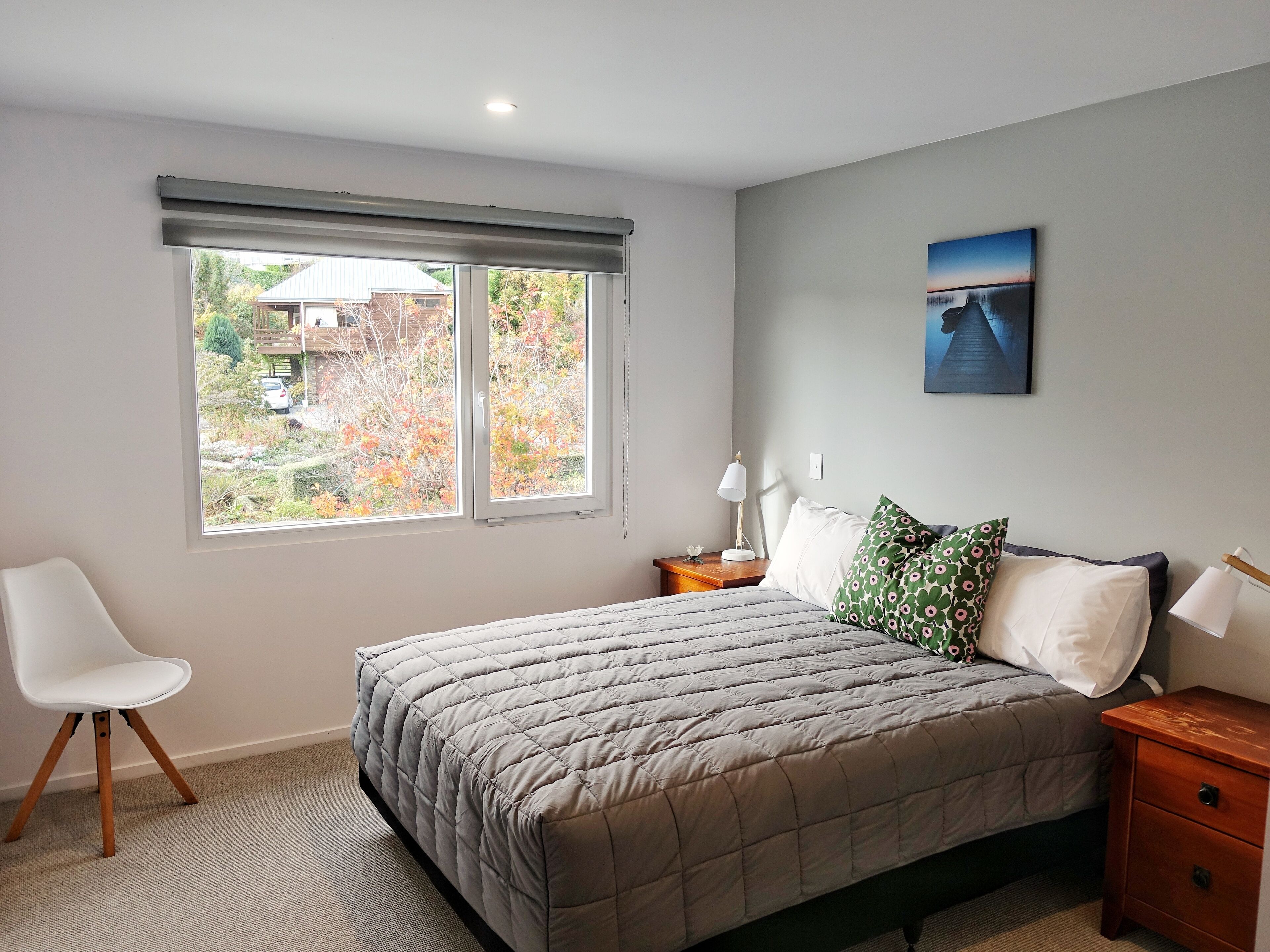 Ein Schlafzimmer mit Bett, Sessel, Nachttisch, Lampe und einem Fenster mit Gartenblick.