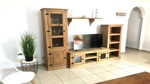 A wooden entertainment unit with a flat-screen TV, glass cabinets, and shelves.