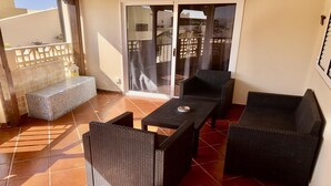 A balcony with a tiled floor, a bench, and two wicker chairs with a table.