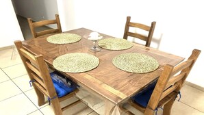 A wooden dining table with four woven placemats, a wine glass, and blue cushioned chairs.