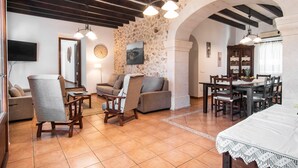 A spacious living room with a stone wall, wooden furniture, and a dining area with a table and chairs. - SES ANGOIXES - Spectacular house in the countryside with private pool and free WiFi (Santanyí)