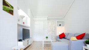 Ett modernt vardagsrum med en grå soffa, en platt-TV, ett litet vitt bord och ett vitt soffbord.