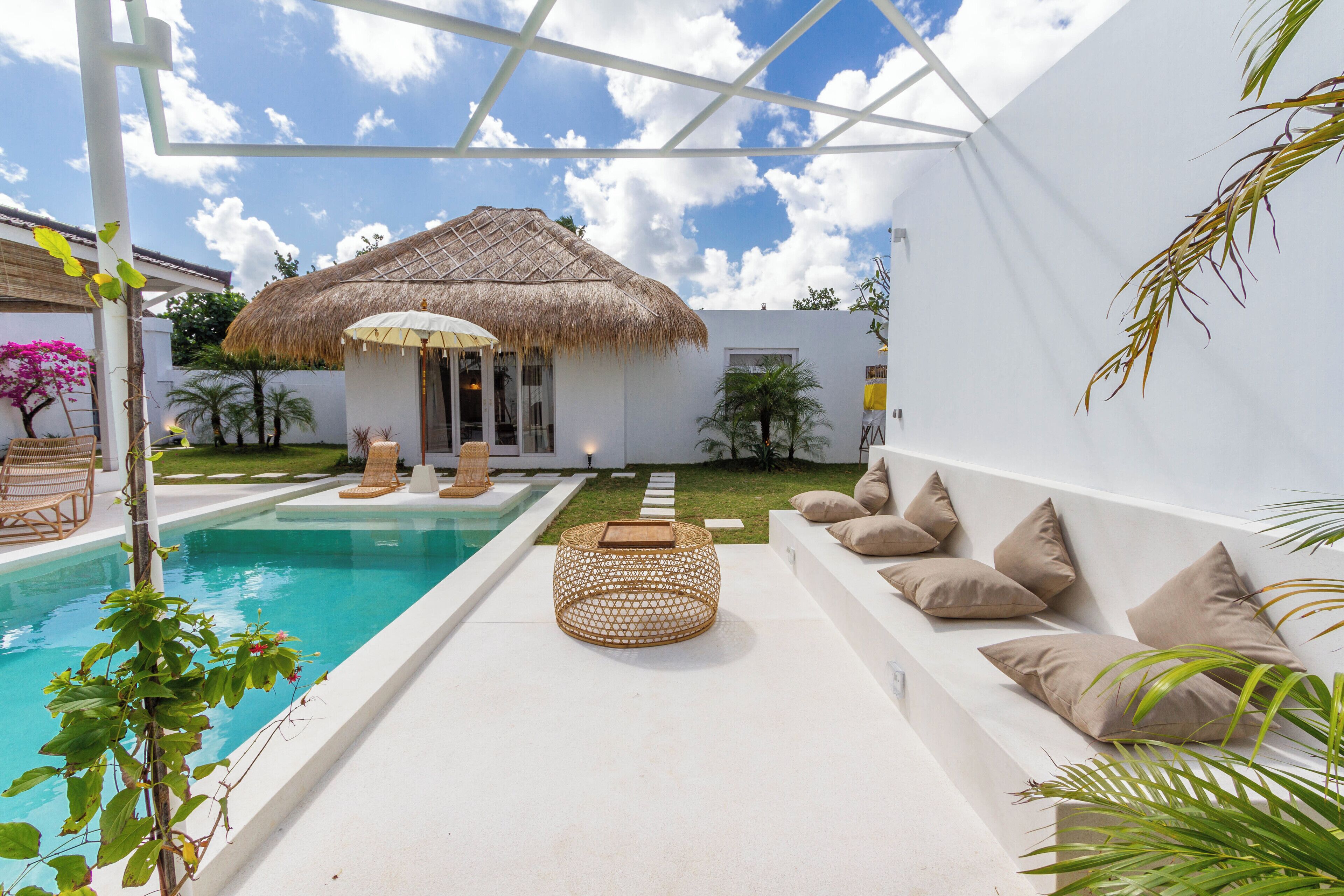 A pool area with a thatched-roof structure, lounge chairs, and a seating area with cushions.