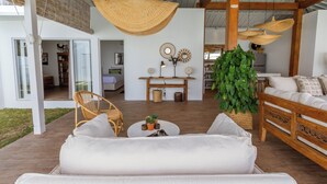 A modern living room with a white sofa, wicker chairs, a coffee table with plants, and a large green plant. - Villa M2 by Alfred in Bali (Seminyak)
