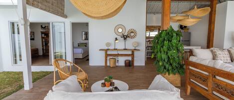 A modern living room with a white sofa, wicker chairs, a coffee table with plants, and a large green plant.