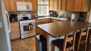 A kitchen with wooden cabinets, a stove, a microwave, and a sink. - No Cleaning Fees, Spacious & Secluded Mountain Home, Pikes Peak Views, Hot Tub! (Cripple Creek)